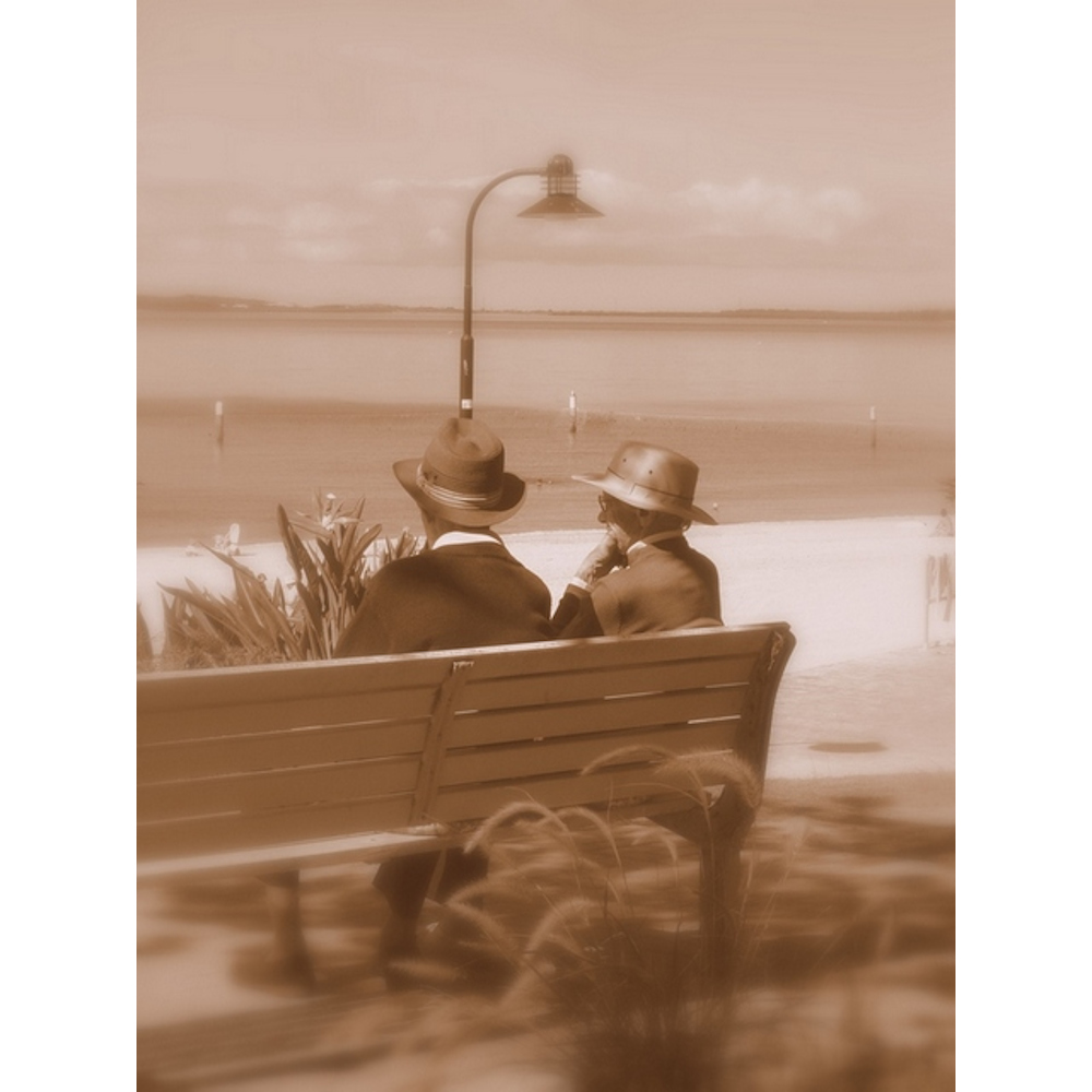 2 elderly men sitting on a bench by the beach
