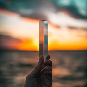 Person holding a rectnagular prism up to evening sky